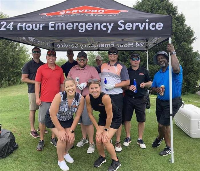 females and males standing in front of servpro tent on golf course